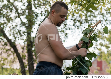 Muscular Man Pruning Tree Branches Outdoors: Bare Torso, Shorts, Green Foliage, Sunny Day, Natural Garden Scene, Realistic Style. 129355832