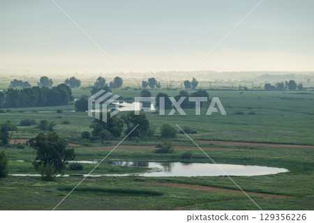 River valley in morning fog, bright sun rays illuminating meadow. Beautiful landscape of river valley in summer River valley in morning fog, bright sun rays illuminating meadow. Beautiful landscape of river valley in summer 129356226