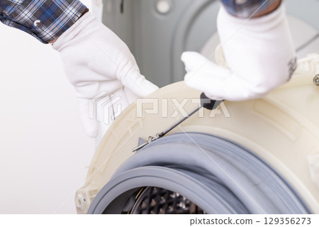 Repairing washer in service centre. Repairman disassembling washer drum, taking off rubber gasket with a screwdriver Repairing washer in service centre. Repairman disassembling washer drum, taking off rubber gasket with a screwdriver 129356273