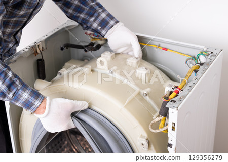 Fixing washing machine. Repairer in white protective gloves installing fixed washing tub drum to washing machine 129356279