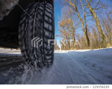 Sunny winter drive on a snowy road surrounded by trees and blue sky. A car maneuvers through road covered with snow on a bright, sunny winter day along a tree-lined road 129356293