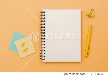 Notebook with yellow pen and push pins on orange desk Notebook with yellow pen and push pins on orange desk 129356370
