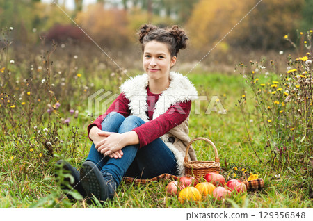 Thanksgiving Vibes. Young girl sitting on blanket in autumn meadow holding two small pumpkins, surrounded by wildflowers. warmth and whimsy of autumn harvest, childhood, and outdoor seasonal fun Thanksgiving Vibes. Young girl sitting on blanket in autumn meadow holding two small pumpkins, surrounded by wildflowers. warmth and whimsy of autumn harvest, childhood, and outdoor seasonal fun 129356848