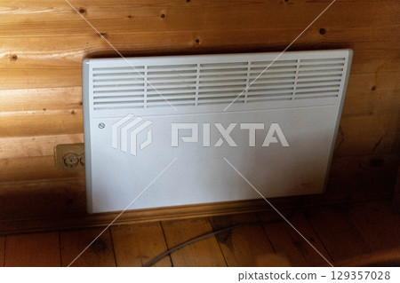 Electric convection heater providing warmth in wooden cabin 129357028