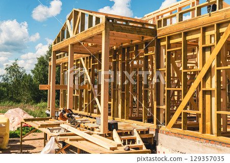 Wooden frame house under construction on sunny summer day 129357035