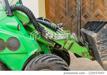 Green tractor arm with hydraulic hoses and bucket ready for work 129357047