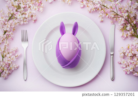 Easter table setting with pink egg wrapped in purple bunny napkin and cherry blossoms 129357201