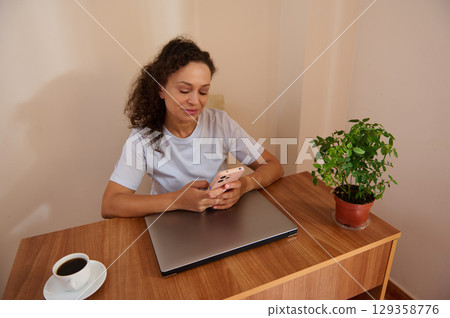 Woman Using Smartphone While Working at Desk in Comfortable Home Setup Woman Using Smartphone While Working at Desk in Comfortable Home Setup 129358776