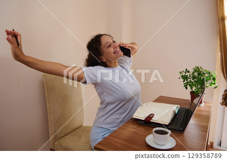 Woman Cheerfully Working from Home With Coffee and Laptop on Desk 129358789