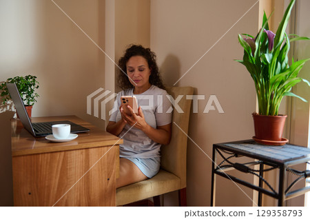 Young Woman Working From Home Using Mobile Phone and Laptop Young Woman Working From Home Using Mobile Phone and Laptop 129358793
