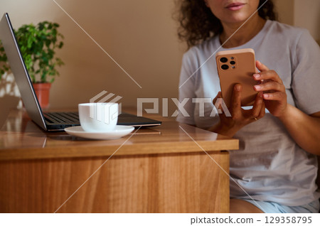 Woman Using Smartphone While Working From Home With Laptop and Coffee Woman Using Smartphone While Working From Home With Laptop and Coffee 129358795