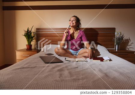 Woman Enjoying Creative Work in a Relaxed Home Bedroom Setting 129358804