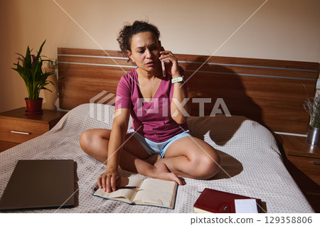 Woman Working Remotely While Talking on Phone in Cozy Home Interior 129358806