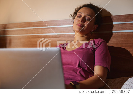 Young Woman Relaxing With a Laptop in a Cozy Bedroom 129358807