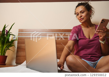 Woman Using Laptop and Phone in Comfortable Home Setting 129358812