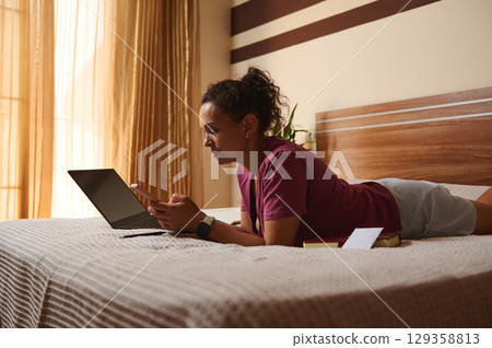 Woman Working Remotely on Laptop in a Cozy Bedroom Interior Woman Working Remotely on Laptop in a Cozy Bedroom Interior 129358813