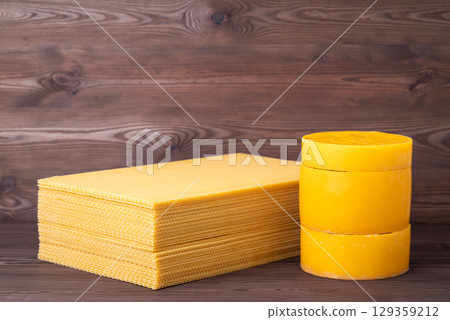 Sheets and cylinders of natural beeswax on wooden background. Yellow wax used for frames in beehive, beekeeping concept 129359212