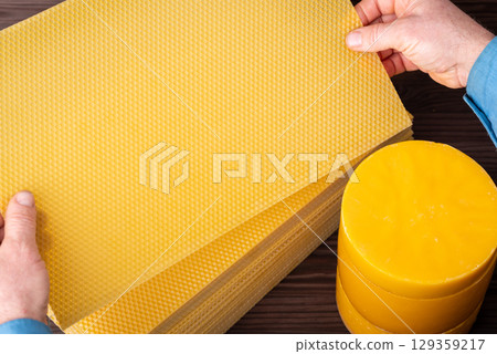 Making new sheets of wax, man looking them through. New sheets of wax made from used one from the hive, stack of wax in cylinders used for making sheets Making new sheets of wax, man looking them through. New sheets of wax made from used one from the hive, stack of wax in cylinders used for making sheets 129359217