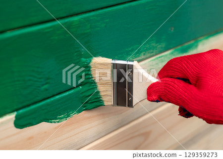 Close up of man hand painting wooden wall. Renovating house outdoor, painting wall in green color 129359273