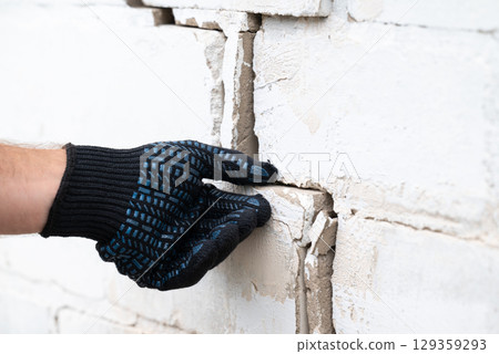 Worker inspecting crack on brick wall before repairing. White brick wall of a building with deep crack Worker inspecting crack on brick wall before repairing. White brick wall of a building with deep crack 129359293
