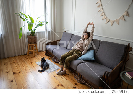 Lethargic woman sitting with lazy stretch, unable to motivate despite having time, cat sleep nearby Lethargic woman sitting with lazy stretch, unable to motivate despite having time, cat sleep nearby 129359353