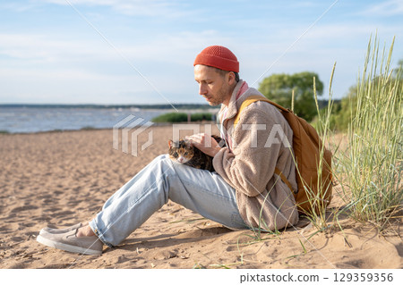Attentive man comfort cat companion while sit on coastal shoreline. Animal travel outdoor adaptation Attentive man comfort cat companion while sit on coastal shoreline. Animal travel outdoor adaptation 129359356