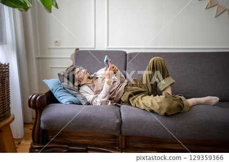 Lazy woman idleness lounging on sofa with smartphone scrolling at home alone, lost in thoughts 129359366