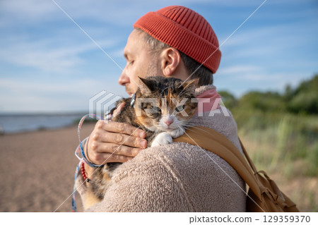 Grumpy frowning sullen cat presses close to male owner during outdoor walk. Reluctant affection Grumpy frowning sullen cat presses close to male owner during outdoor walk. Reluctant affection 129359370