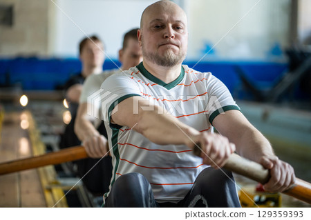 Focused forced rowing athletes train intensely on rowing simulator during synchronized team workout 129359393