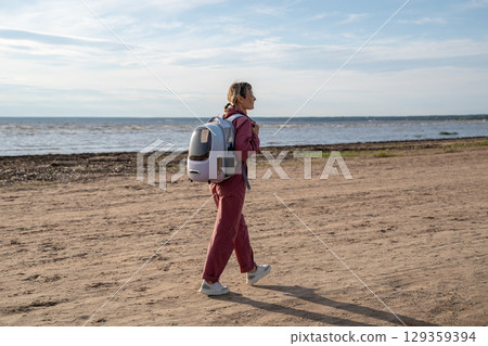 Vacation with pet. Calm woman with backpack carrier for cat walking on sandy beach by sea shore 129359394