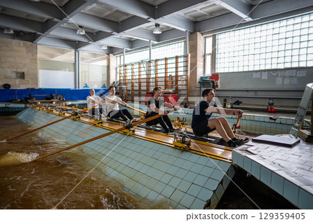 Concentrated tired athletes stroking on rowing simulator. Synchronization, water aquatic sports Concentrated tired athletes stroking on rowing simulator. Synchronization, water aquatic sports 129359405