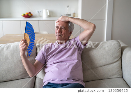 Older man struggling with fan heat exhaustion. Pensioner try to cope in sweltering home in summer 129359425