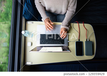 Woman working on laptop while traveling. Computer and smartphone connected to power bank, top view. Woman working on laptop while traveling. Computer and smartphone connected to power bank, top view. 129359429