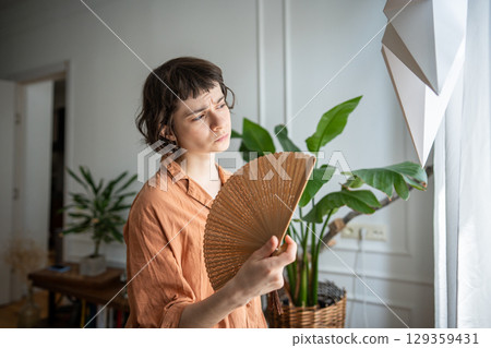 Frustrated woman struggling with sweltering weather fanning herself at home in summer heat 129359431