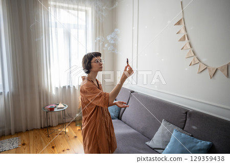 Woman holding fragrant palo santo stick, using smoke for meditation and aromatherapy at cozy home.  129359438