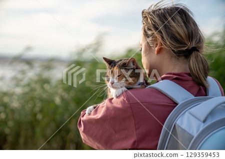 Relaxed cat resting in woman hands during outdoor journey in nature. Pet care safety in travel trip Relaxed cat resting in woman hands during outdoor journey in nature. Pet care safety in travel trip 129359453