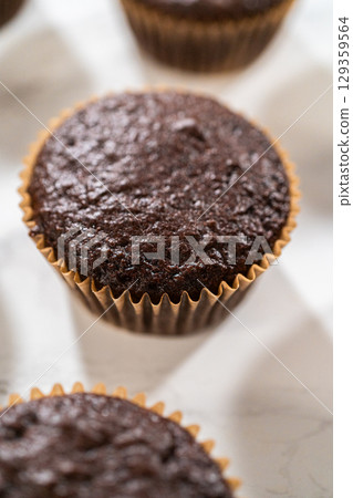 Freshly baked chocolate cupcakes are poised for a delightful transformation as they await a generous coating of rich and velvety chocolate frosting. Freshly baked chocolate cupcakes are poised for a delightful transformation as they await a generous coating of rich and velvety chocolate frosting. 129359564