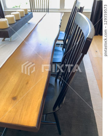 A close-up angle of a natural wooden dining table paired with black spindle chairs. The dining area features a neutral rug and bright daylight from large windows. 129359573