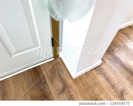 Interior view of a clean white door corner featuring detailed white trim and wood-style vinyl flooring. Ideal for real estate, renovation, or flooring design projects. Keywords include door corner Interior view of a clean white door corner featuring detailed white trim and wood-style vinyl flooring. Ideal for real estate, renovation, or flooring design projects. Keywords include door corner 129359577