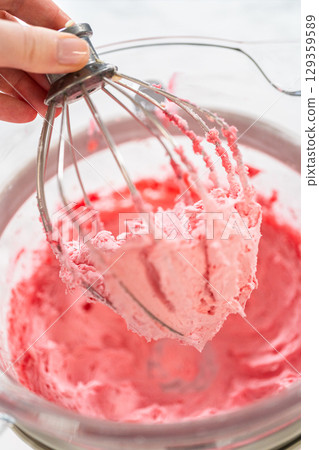 A hand holds a mixer whisk covered in freshly whipped cranberry buttercream. The smooth, airy texture and vibrant pink hue make it a perfect filling or frosting for cookies and cakes. A hand holds a mixer whisk covered in freshly whipped cranberry buttercream. The smooth, airy texture and vibrant pink hue make it a perfect filling or frosting for cookies and cakes. 129359589