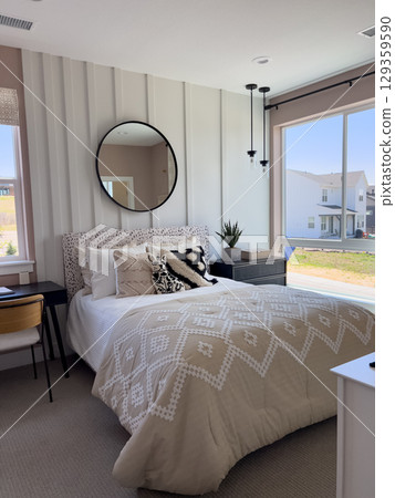 Modern guest bedroom with a decorative round mirror above the bed, pendant lights, and layered pillows. The space is well-lit and tastefully styled. Modern guest bedroom with a decorative round mirror above the bed, pendant lights, and layered pillows. The space is well-lit and tastefully styled. 129359590
