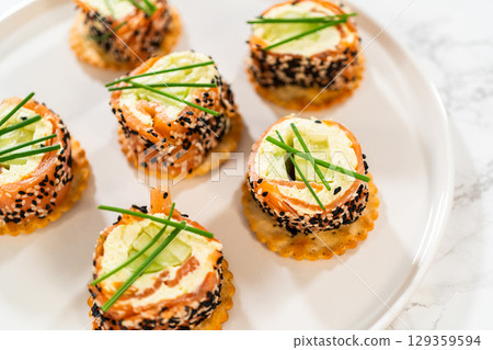 A beautifully plated presentation of smoked salmon jumbo cream cheese rolls on a round white plate. Each roll is sliced to reveal the creamy filling, accented by cucumber slices and wrapped in smoked A beautifully plated presentation of smoked salmon jumbo cream cheese rolls on a round white plate. Each roll is sliced to reveal the creamy filling, accented by cucumber slices and wrapped in smoked 129359594