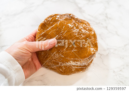 Close-up of a single portion of Zesty Orange Gingerbread Cookie Dough wrapped in plastic wrap, ready to be chilled. The smooth dough surface hints at a rich, flavorful result after baking. Close-up of a single portion of Zesty Orange Gingerbread Cookie Dough wrapped in plastic wrap, ready to be chilled. The smooth dough surface hints at a rich, flavorful result after baking. 129359597