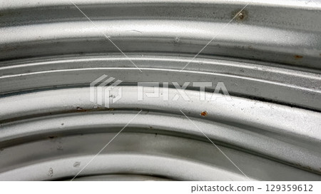 A close-up of a galvanized metal basement window well wall, showing curved horizontal ridges and metallic texture. The surface is clean and well-maintained. 129359612