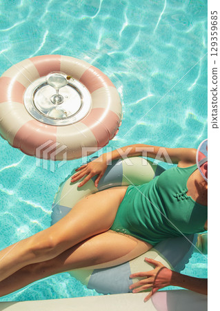 Woman relaxing on inflatable ring in clear swimming pool under bright sunlight Woman relaxing on inflatable ring in clear swimming pool under bright sunlight 129359685