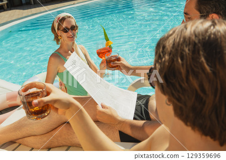Friends relaxing by poolside with summer drinks and newspaper under bright sunlight Friends relaxing by poolside with summer drinks and newspaper under bright sunlight 129359696