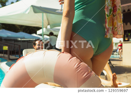 Rare view of woman in green swimsuit holding inflatable ring at poolside Rare view of woman in green swimsuit holding inflatable ring at poolside 129359697