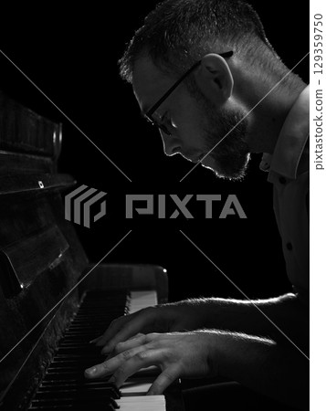 Focused man in glasses playing piano in dark monochrome lighting 129359750