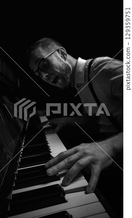 Expressive man in glasses playing piano with wide open mouth in dramatic black and white light 129359751