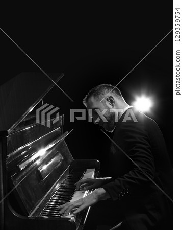 Male pianist in tuxedo performing on piano under bright stage light Male pianist in tuxedo performing on piano under bright stage light 129359754